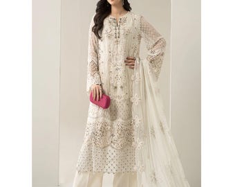May include: An ivory-colored, embroidered formal outfit. The ensemble includes a long-sleeved tunic with intricate detailing, wide-leg pants, and a matching sheer scarf. A pink clutch and red heels complete the look.
