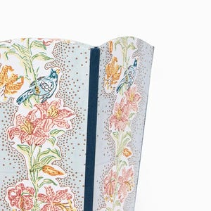 May include: A section of a decorative screen featuring a floral and bird pattern. The design includes pink and orange lilies, blue birds, and green foliage on a light blue background with brown dots. A dark blue border is visible.