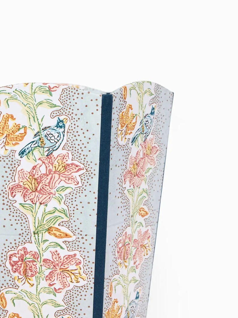 May include: A section of a decorative screen featuring a floral and bird pattern. The design includes pink and orange lilies, blue birds, and green foliage on a light blue background with brown dots. A dark blue border is visible.