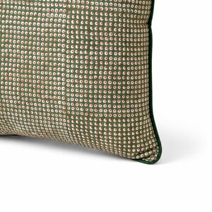 May include: A decorative pillow with a green background and a pattern of small white and red circles. The pillow has a dark green border, and the fabric appears to be a soft material. The pillow is designed for home decor.