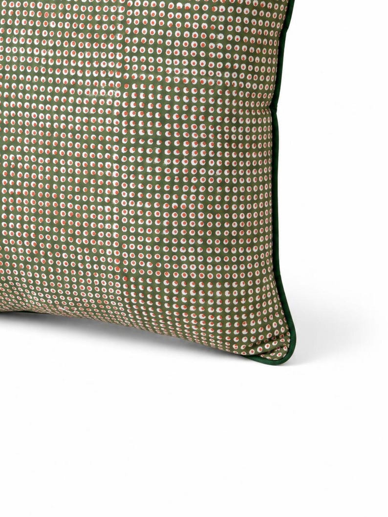 May include: A decorative pillow with a green background and a pattern of small white and red circles. The pillow has a dark green border, and the fabric appears to be a soft material. The pillow is designed for home decor.