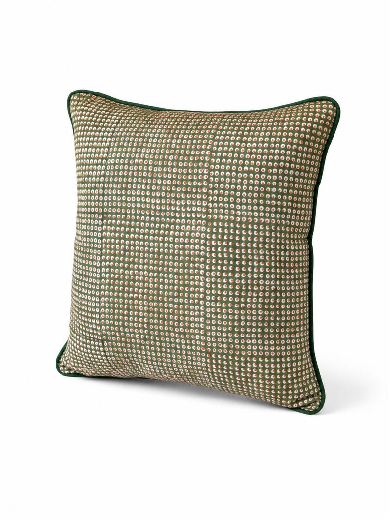 May include: Square decorative pillow with a green and white dot pattern. The pillow has a dark green border. The pattern is a repeating series of small dots in white, green, and red. The pillow is a square shape.