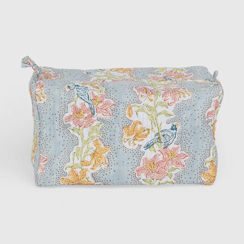 May include: A rectangular, light blue cosmetic bag with a floral and bird pattern. The design features pink, yellow, and green flowers with blue birds. The bag has a zipper closure and a small loop on one side.