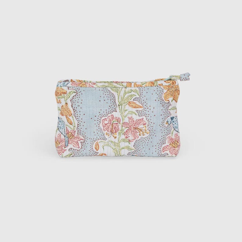 May include: A small, rectangular floral print pouch with a zipper closure. The pouch features a light blue background with a pattern of pink, orange, and blue flowers and leaves. The zipper pull is a small fabric loop.