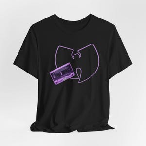 May include: Black t-shirt featuring a purple Wu-Tang Clan logo and a purple cassette tape graphic. The design is centered on the front of the shirt. The shirt is made of a soft material.