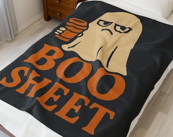 May include: Black blanket with an orange "BOO SHEET" text design and a cartoon ghost holding a coffee cup. The ghost has an angry expression. The blanket is on a bed with a white pillow.