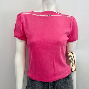 May include: A bright pink short-sleeved top with a white trim along the neckline and sleeves. The top is displayed on a mannequin. A tag that says "Lady Vanderbilt" is attached to the top.
