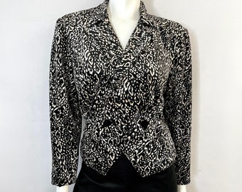 May include: A black and white patterned blazer with a double-breasted design. The blazer has long sleeves and a notched collar. The outfit includes black pants. The clothing is displayed on a mannequin.