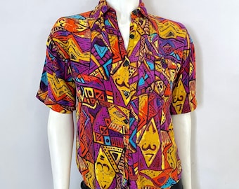 Puede incluir: Una camisa de manga corta con un llamativo diseño geométrico en tonos amarillos, naranjas, morados y azules. La camisa se exhibe en un maniquí, resaltando su colorido patrón y ajuste a medida. Cuenta con un cuello clásico y cierre de botones.