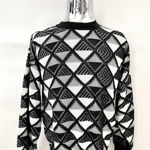 May include: Black and white geometric pattern sweater. The sweater features a repeating diamond design in black and white. The sweater has a crew neck and long sleeves with black cuffs. The bottom hem is also black.
