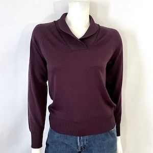 Pode incluir: Um suéter cor de ameixa com gola xale e mangas compridas. A gola e os punhos canelados proporcionam um contraste de textura. O suéter é exibido em um manequim, combinado com jeans azul.