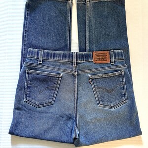 May include: Blue denim jeans with a classic five-pocket design. The jeans feature a brown leather patch with the Levi Strauss & Co. logo on the back waistband. The jeans are folded, showcasing the back pockets and stitching details.