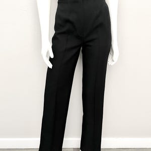 May include: High-waisted black trousers featuring a straight-leg silhouette, a clean waistband with a single centered button closure, and a subtle pressed crease running down the center of each leg, providing a structured and tailored appearance.