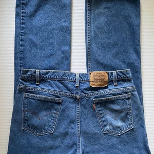 May include: Blue denim jeans with a classic five-pocket design. The jeans have a straight leg cut and a brown leather patch with the Levi Strauss & Co. logo. The back pockets feature the signature Levi's stitching.