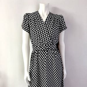 May include: A black and white patterned dress with a wrap-style design. The dress features short sleeves and a V-neckline. A matching belt cinches the waist. The fabric has a repeating pattern of black shapes on a white background.