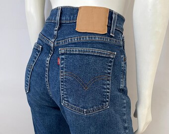 May include: Dark wash denim jeans with a high waist and a classic five-pocket design. The jeans feature a brown leather patch on the back waistband and the iconic Levi's red tab on the back pocket. The jeans are displayed on a mannequin.