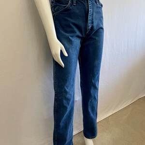 May include: Dark wash denim jeans with a classic straight leg fit. The jeans feature a button and zipper closure, front and back pockets, and belt loops. The jeans are displayed on a mannequin.