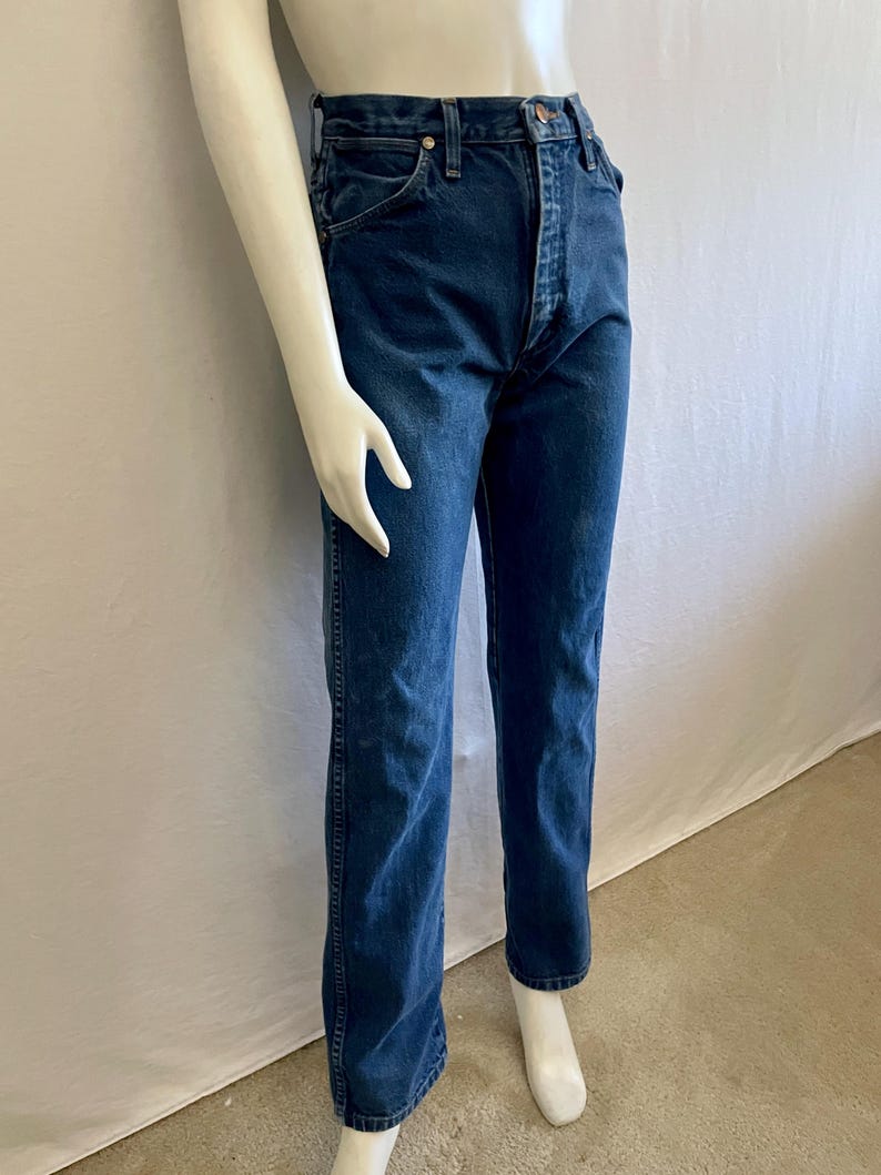 May include: Dark wash denim jeans with a classic straight leg fit. The jeans feature a button and zipper closure, front and back pockets, and belt loops. The jeans are displayed on a mannequin.