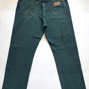 May include: Dark teal Wrangler jeans, viewed from the back, showcasing the pockets, belt loops, and a leather patch. The jeans have a classic five-pocket design and a straight leg cut. The denim appears to be a medium weight.