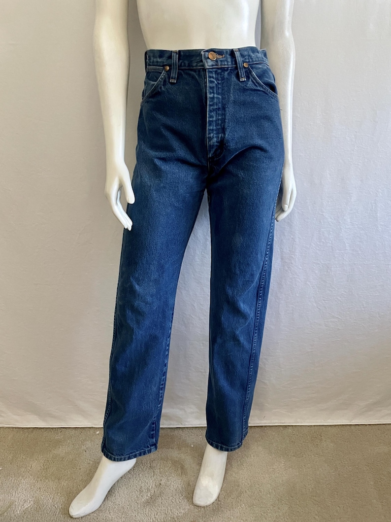 May include: Dark blue denim jeans with a button and zipper closure. The jeans have a classic five-pocket design and a straight leg fit. The jeans are displayed on a mannequin.