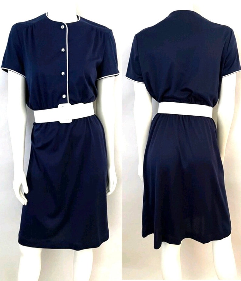 Op de afbeelding: Een marineblauwe jurk met korte mouwen, witte bies en een witte riem. De jurk heeft een knoopsluiting aan de voorkant en een knielange rok. De jurk wordt op een mannequin getoond.