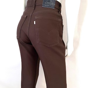 May include: Brown high-waisted pants with a classic five-pocket design. The pants feature a dark brown color, a leather patch with "silver tab" text, and a small white tag on the back pocket. The pants are made of a smooth fabric.