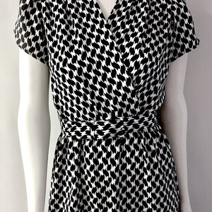 May include: A black and white patterned dress with a V-neckline and short sleeves. The dress features a wrap-style bodice and a cinched waist. The pattern is a repeating design of curved shapes.