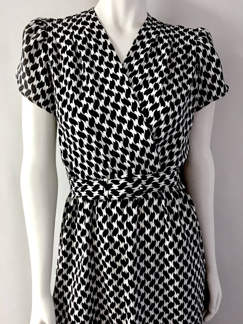 May include: A black and white patterned dress with a V-neckline and short sleeves. The dress features a wrap-style bodice and a cinched waist. The pattern is a repeating design of curved shapes.