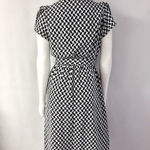 May include: A black and white patterned dress with short sleeves and a tie waist. The dress features a repeating pattern of black shapes on a white background. The dress is displayed on a mannequin.