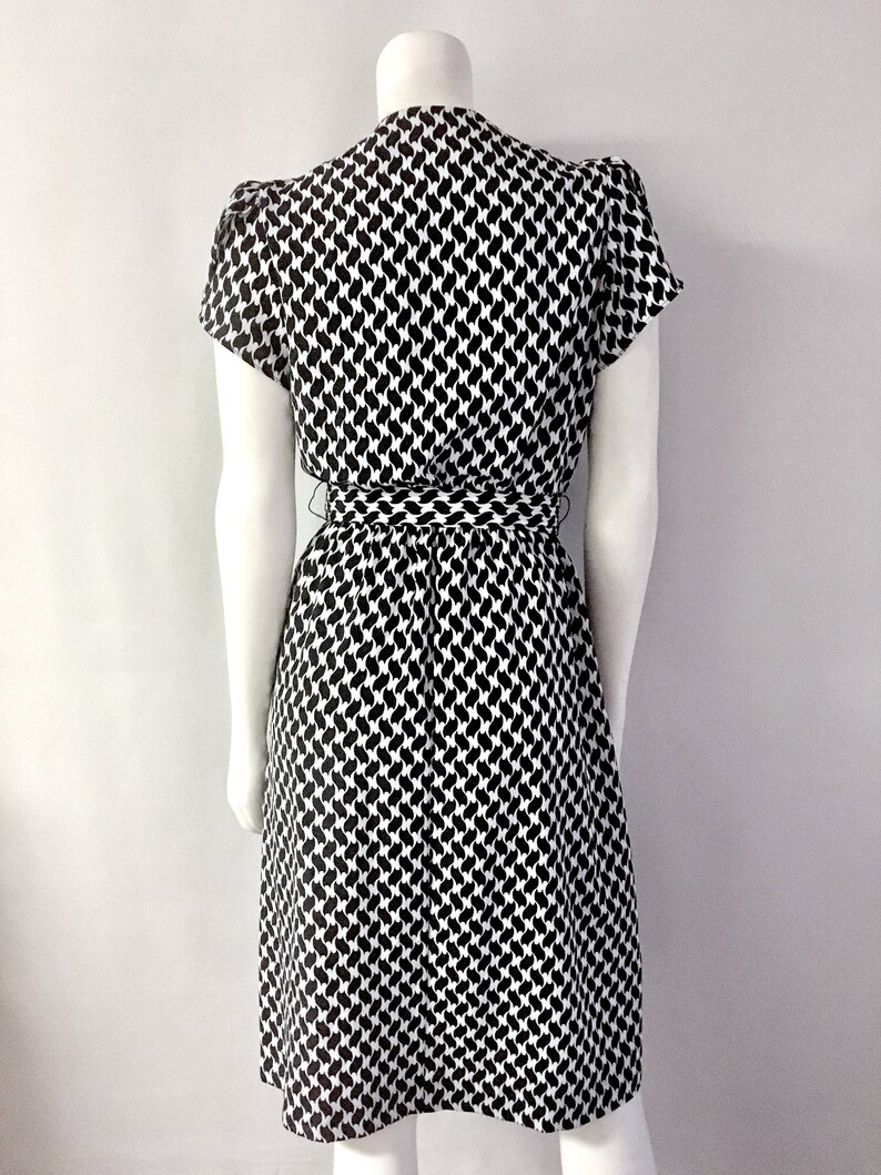 May include: A black and white patterned dress with short sleeves and a tie waist. The dress features a repeating pattern of black shapes on a white background. The dress is displayed on a mannequin.