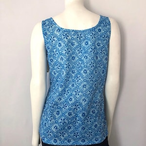 May include: A sleeveless tank top with a blue floral pattern. The top has a scoop neckline and is made of a lightweight fabric. The floral design features small, stylized flowers and leaves in varying shades of blue.