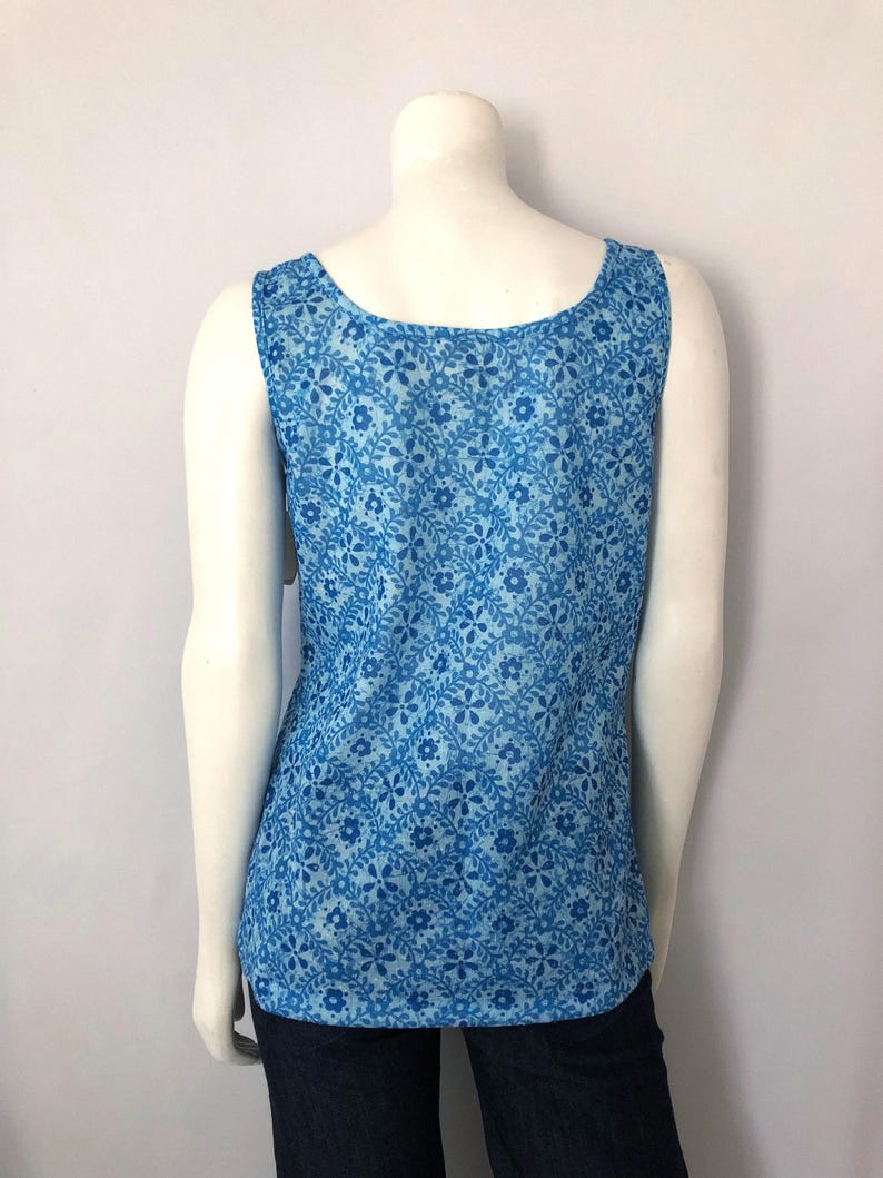 May include: A sleeveless tank top with a blue floral pattern. The top has a scoop neckline and is made of a lightweight fabric. The floral design features small, stylized flowers and leaves in varying shades of blue.
