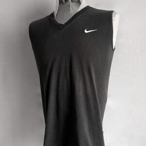 Puede incluir: Una camiseta sin mangas gris oscuro con cuello en V. La camiseta presenta un peque&ntilde;o logotipo blanco de Nike en la parte superior izquierda del pecho. La prenda se exhibe en un maniqu&iacute;.