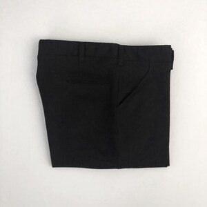 May include: Folded black dress pants with a button and zipper closure, belt loops, and pockets. The pants are made of a smooth, solid black fabric and are neatly folded on a white background.