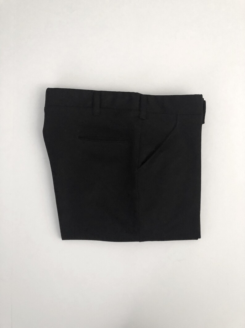 May include: Folded black dress pants with a button and zipper closure, belt loops, and pockets. The pants are made of a smooth, solid black fabric and are neatly folded on a white background.