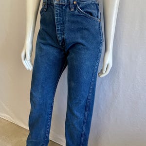 May include: Blue denim jeans with a button fly and classic five-pocket design. The jeans are displayed on a mannequin, showcasing the straight-leg fit and the details of the stitching and hardware.