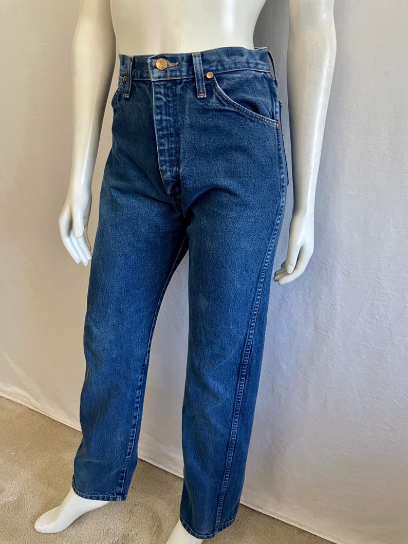 May include: Blue denim jeans with a button fly and classic five-pocket design. The jeans are displayed on a mannequin, showcasing the straight-leg fit and the details of the stitching and hardware.