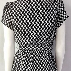 May include: A black and white patterned dress with short sleeves and a cinched waist. The dress features a repeating abstract design. The dress is displayed on a mannequin.