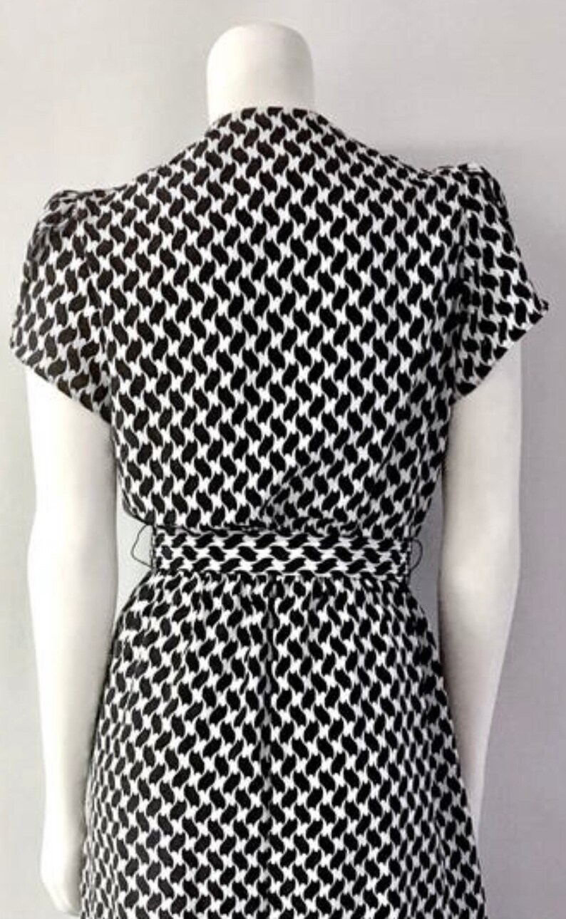 May include: A black and white patterned dress with short sleeves and a cinched waist. The dress features a repeating abstract design. The dress is displayed on a mannequin.