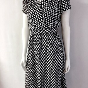 May include: A black and white patterned dress with a wrap-style bodice and short sleeves. The dress features a cinched waist and a knee-length skirt. The fabric has a repeating pattern of black shapes on a white background.
