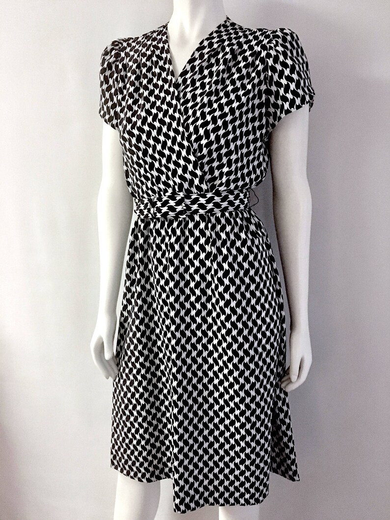 May include: A black and white patterned dress with a wrap-style bodice and short sleeves. The dress features a cinched waist and a knee-length skirt. The fabric has a repeating pattern of black shapes on a white background.