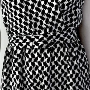 May include: A black and white patterned dress with a wrap-style bodice and a cinched waist. The dress features a repeating abstract design. The fabric appears to be lightweight, suitable for warmer weather.