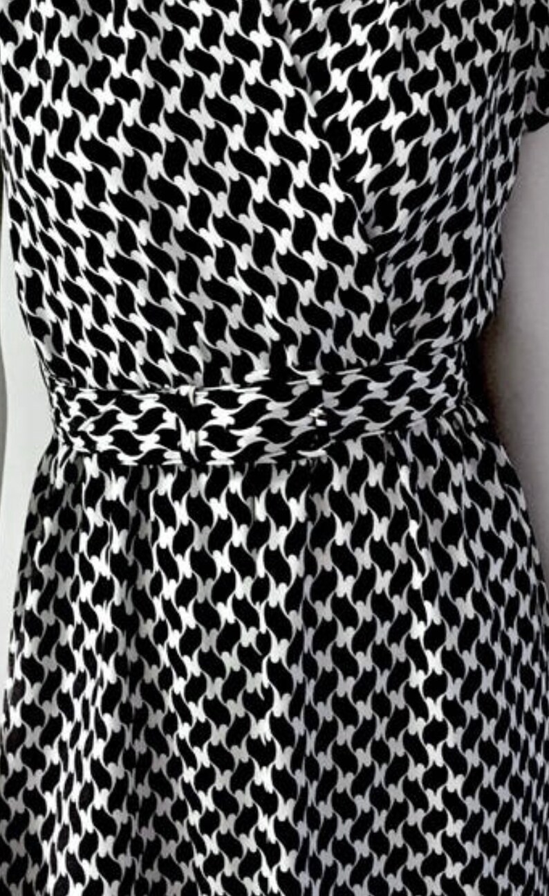 May include: A black and white patterned dress with a wrap-style bodice and a cinched waist. The dress features a repeating abstract design. The fabric appears to be lightweight, suitable for warmer weather.