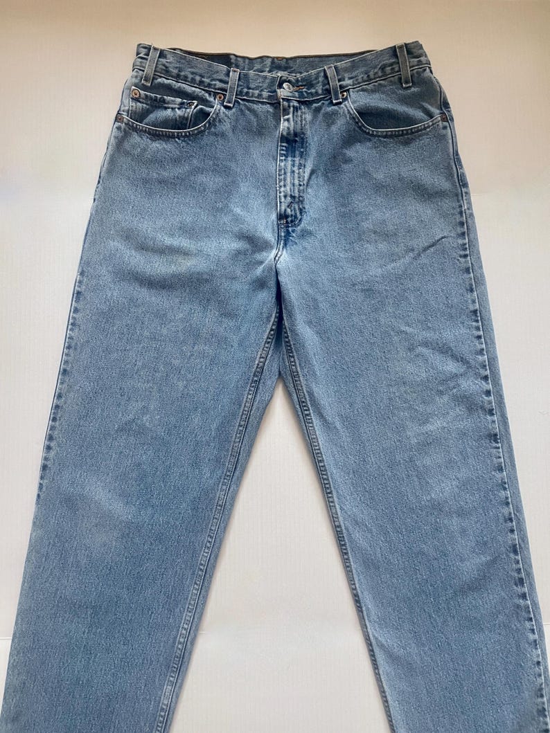May include: Light blue denim jeans with a classic five-pocket design. The jeans have a straight leg cut and a button and zipper closure. The denim has a faded appearance, with visible stitching details.