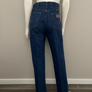 May include: Dark blue denim jeans with a classic fit. The jeans feature a high waist, back pockets, and a brown leather patch. The jeans are displayed on a mannequin. The jeans are a classic style.