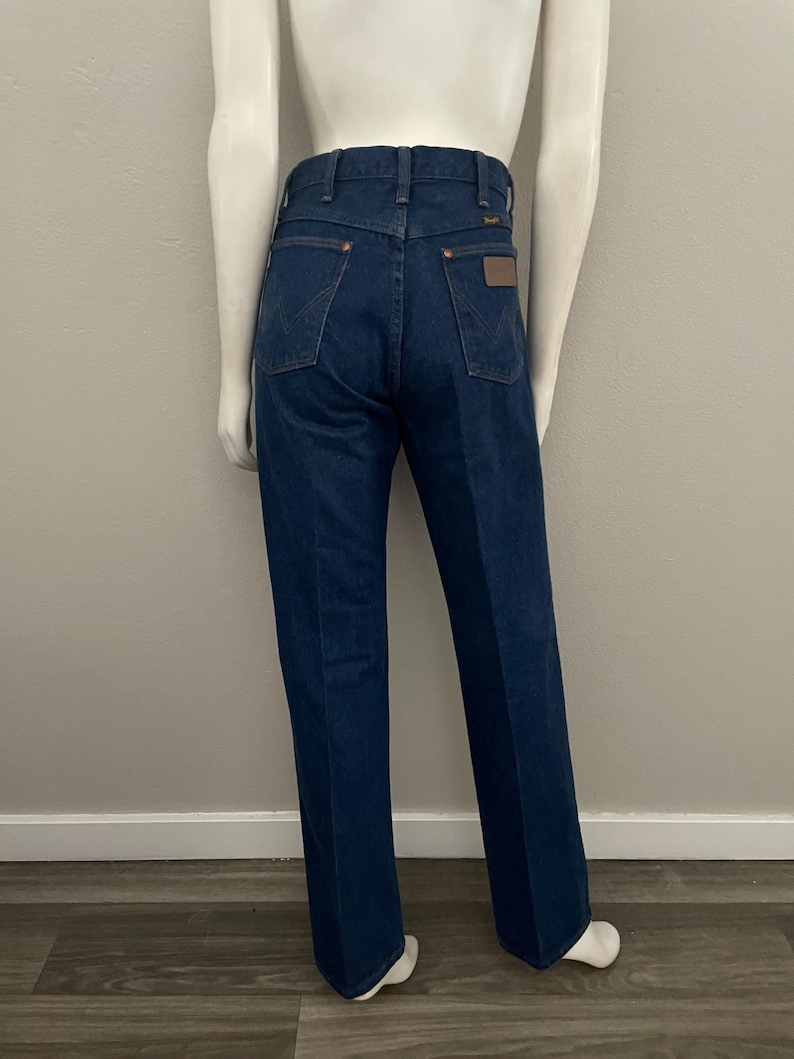 May include: Dark blue denim jeans with a classic fit. The jeans feature a high waist, back pockets, and a brown leather patch. The jeans are displayed on a mannequin. The jeans are a classic style.