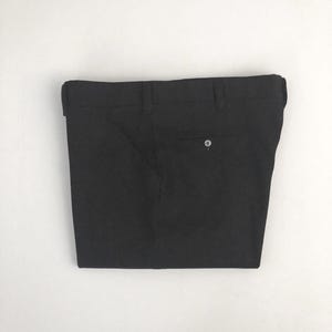 May include: Black dress pants with a button closure and belt loops. The pants are folded and displayed against a white background. The pants have two back pockets.