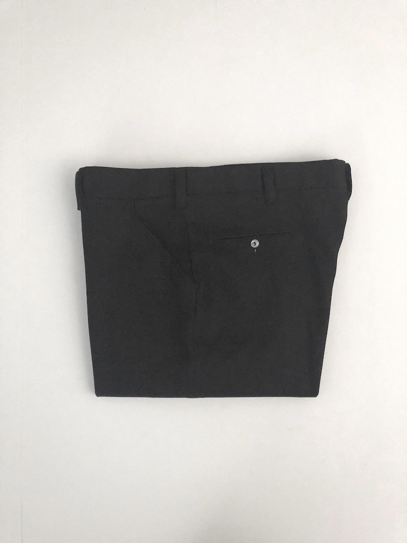 May include: Black dress pants with a button closure and belt loops. The pants are folded and displayed against a white background. The pants have two back pockets.