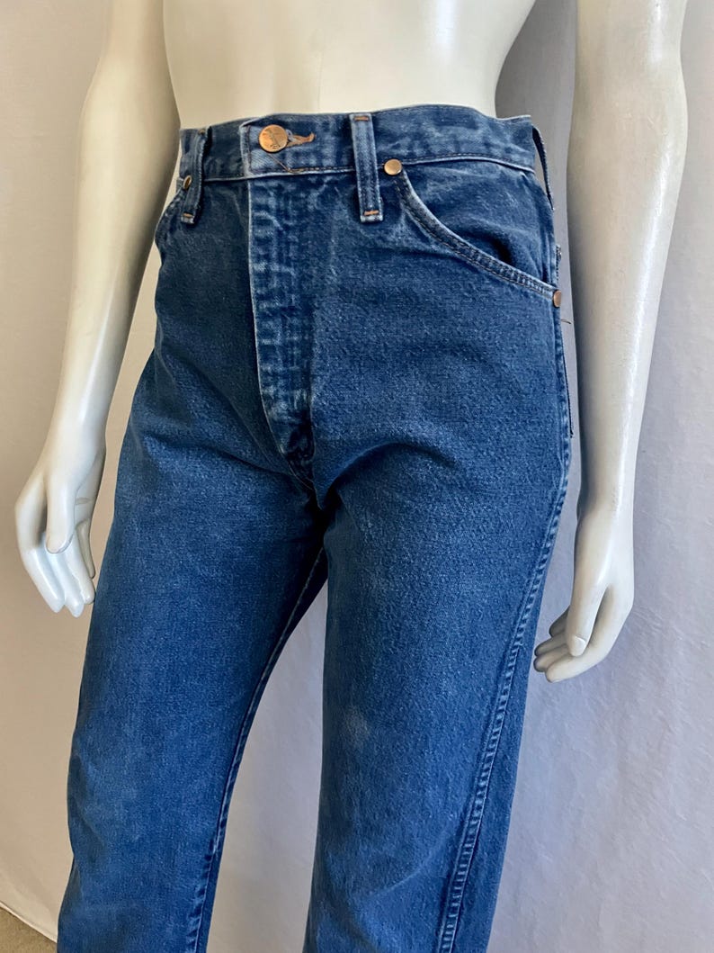 May include: Blue denim jeans with a classic five-pocket design. The jeans feature a button and zipper closure, belt loops, and copper-colored rivets. The denim has a medium wash with subtle fading and wear.