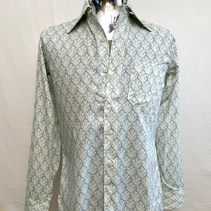 Op de afbeelding: Een lange mouwen overhemd met een blauw bloemmotief op een crèmekleurige achtergrond. Het overhemd heeft een klassieke kraag, een borstzak en wordt op een mannequin gepresenteerd.